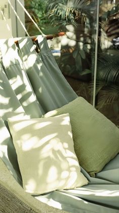 a hammock with two pillows on it in front of some plants and trees