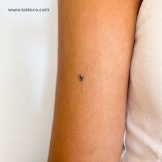 a woman's arm with a small tattoo of a dandelion on it