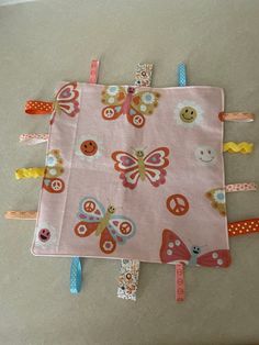 a pink blanket with colorful butterflies and buttons on it, sitting on the floor next to a pair of scissors