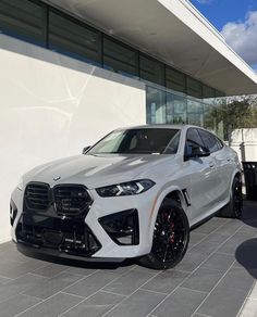 a white bmw suv is parked in front of a building with black wheels and rims