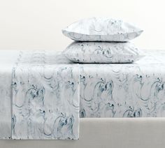 two pillows are on top of a bed with white sheets and blue marbled designs