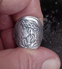 a person holding a silver coin in their left hand and wearing a ring with the image of jesus on it