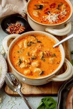 two bowls of soup on a cutting board with silver spoons and other food items