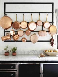 pots and pans are hanging on the wall above an oven with marble countertops