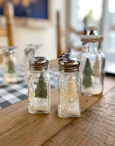 three glass jars filled with small trees on top of a wooden table