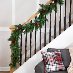 a christmas garland is hanging on the bannister next to a stair case with red and green plaid pillows