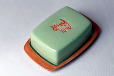 an orange and green plate with a cow design on the front is sitting on a white surface