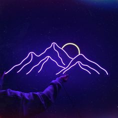 a person holding up a neon sign with mountains in the background and a heart on it