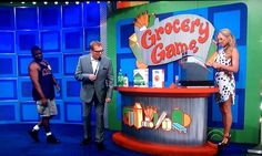 two men and a woman are standing in front of a game stand on tv set