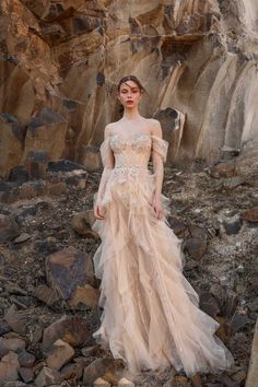 a woman standing on rocks wearing a dress with long sleeves and an off the shoulder design