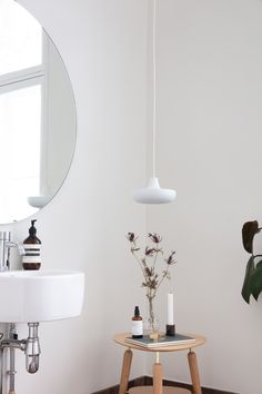 a white bathroom with a wooden table and round mirror on the wall next to it