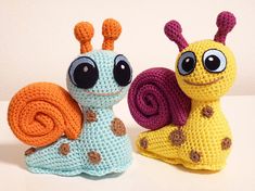 two crocheted snails sitting next to each other on a white surface with one snail looking at the camera