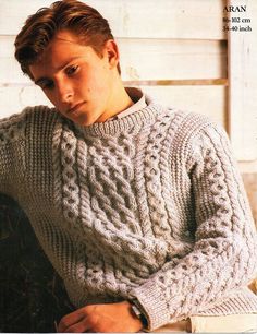 a young man wearing a cabled sweater sitting on a bench