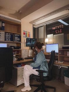 a woman sitting at a desk in front of a computer monitor and two monitors on the wall