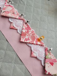 a pink and white quilted table runner with several pieces of fabric hanging from it