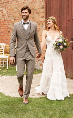 the bride and groom are walking together in front of an old brick building holding hands