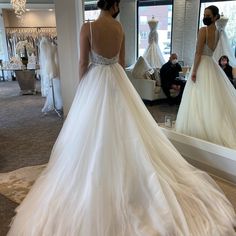 a woman in a white wedding dress looking at herself in the mirror while another person sits nearby