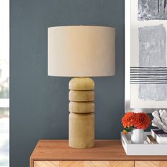 a table lamp sitting on top of a wooden dresser next to a painting and vase