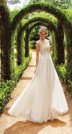 a woman in a wedding dress is walking through an archway with greenery on either side