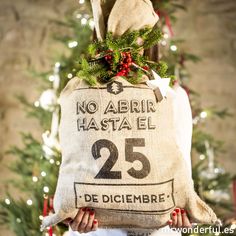 a woman holding a bag with the number 25 on it in front of a christmas tree