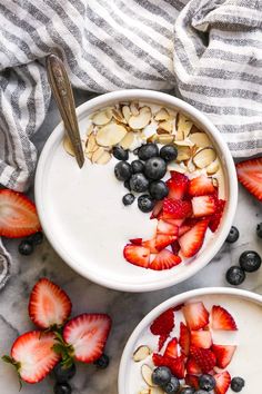 two bowls filled with yogurt, strawberries and almonds on a marble surface