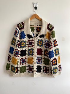 a colorful crocheted jacket hanging on a white wall next to a wooden hanger