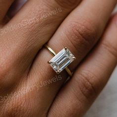 a woman's hand with a diamond ring on her left hand and an emerald stone in the middle