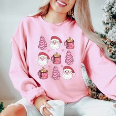 This cute, festive Christmas sweatshirt features adorable Christmas Tree cakes, retro Santa and a cute cup of hot coca. This Christmas crewneck would be the perfect addition to any Holiday wardrobe. Check out more designs here: www.etsy.com/shop/jadeandroseshop ❤️ Please note that for the oversized look you need to buy 1-3 sizes larger than you normally wear. If you prefer the standard Unisex fit order your typical size. For women, if you prefer a more women's fit sweatshirt please size down 1 s Cute Pink Christmas Tops, Cozy Crew Neck Top For Christmas, Cute Holiday Crew Neck Sweatshirt, Cute Crew Neck Sweatshirt For Holiday, Cute Winter Tops As Gift, Cute Winter Tops As A Gift, Pink Tops As Winter Gifts, Cute Christmas Sweatshirt With Graphic Print, Cute Christmas Graphic Print Sweatshirt