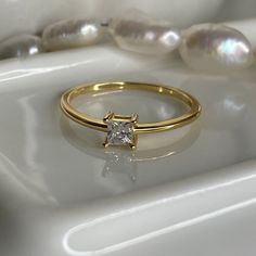 a gold ring with a princess cut diamond in the center and pearls on the side