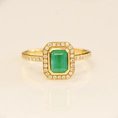 an emerald and diamond ring on a white surface