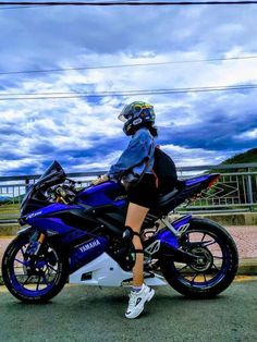 a woman sitting on the back of a blue and white motorcycle in front of a cloudy sky