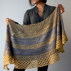 a woman holding up a shawl made from crochet