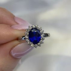 a woman's hand holding a ring with an oval blue stone surrounded by diamonds