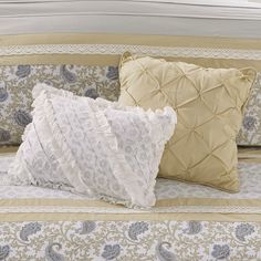 two decorative pillows on a bed with white and gold linens, one in the foreground