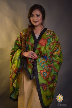 a woman wearing a green and yellow shawl with flowers on it, standing in front of a gray background