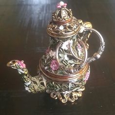 a metal teapot with flowers on it sitting on a table