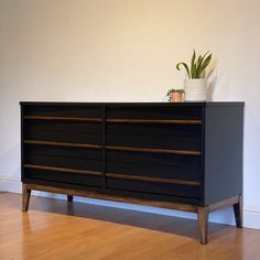 a black dresser sitting on top of a hard wood floor next to a white wall