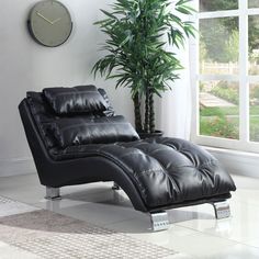 a black leather chaise lounge chair in front of a window with a clock on the wall