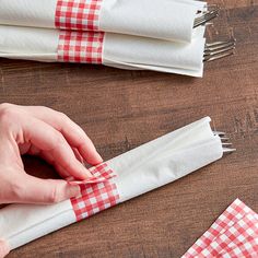 someone is making napkins with red and white gingham cloth on them,