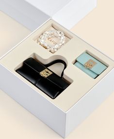 a white box with a black purse and other items in it on top of a table