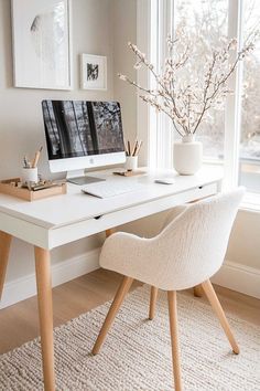 a white desk with a computer on top of it next to a vase filled with flowers