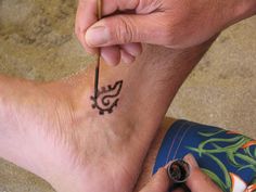 a man is drawing on the foot of another person with a pencil and ink pen