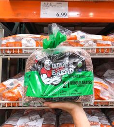 a person holding up a bag of bread in front of some shelves with oranges