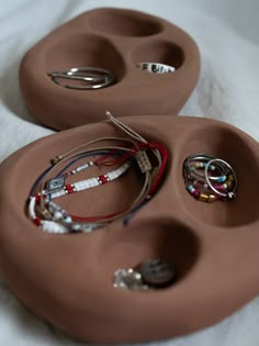 two brown trays with rings and bracelets in them sitting on a white sheet