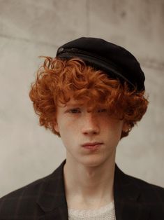 a young man with red curly hair wearing a black beret and looking at the camera