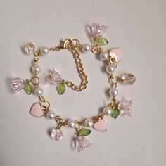 This bracelet is 7.5 inches long with a 2.6-inch extender. It has gold links, pink flower charms with green leaf accents, pink heart charms, and faux pearls. The clasp is a gold lobster clasp. Pink Charm Bracelet, Fairycore Coquette, Pink Charm, Flower Charm, Green Leaf, Jewellery Making, Pink Flower, Pink Heart, Heart Charm