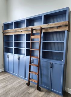 an empty room with blue bookcases, ladder and wooden shelves in the middle