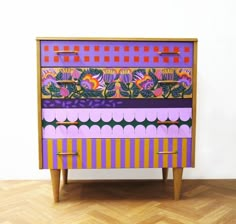 a colorful chest of drawers sitting on top of a hard wood floor next to a white wall