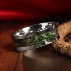 two wedding bands with green moss inlays sitting on top of a wooden table