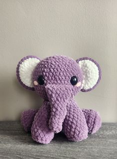 a crocheted purple elephant sitting on top of a wooden table next to a white wall